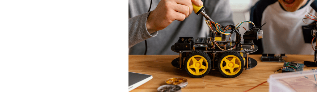 Personne soudant un robot à roues jaunes sur une table