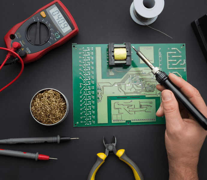 Main tenant un fer à souder sur une carte électronique avec multimètre